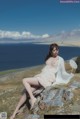 A woman sitting on top of a rock next to the ocean.